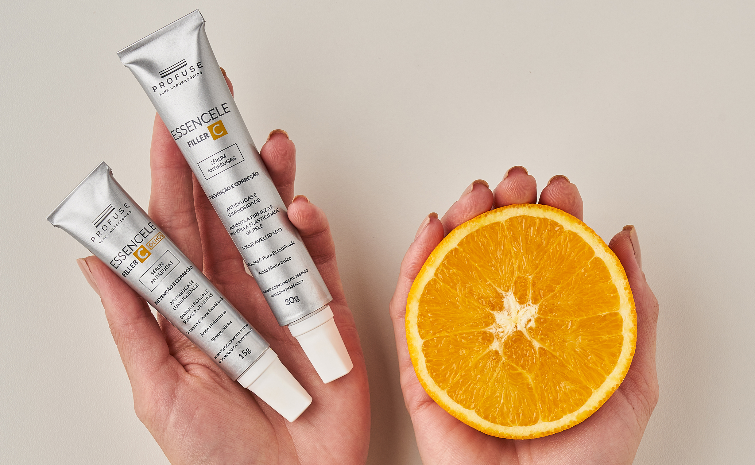 Modelo segurando em uma mão Essencele Filler C e Essencele Filler C Olhos e em outra mão metade de uma laranja